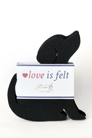 A black felt dog-shaped coaster with a  white branded card that reads 'love is felt' and 'Studio C Collars', photographed on a clean white background.