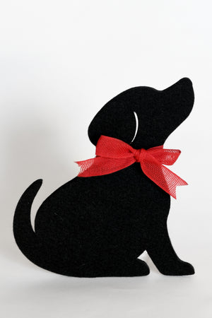 A black felt dog silhouette coaster dog is wearing a red ribbon bow, set against a plain white background.