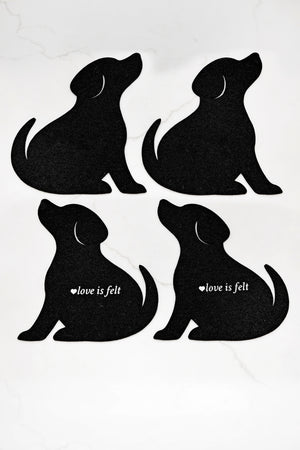 Four black dog silhouette coasters arranged in a 2x2 grid on a white marble background. Two dogs have the white text 'love is felt' printed on their sides.