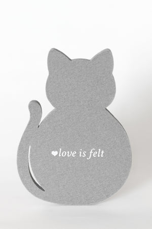 A gray cat-shaped decorative coaster viewed from the back, with the phrase "love is felt" printed in white near the center, on a plain white background.