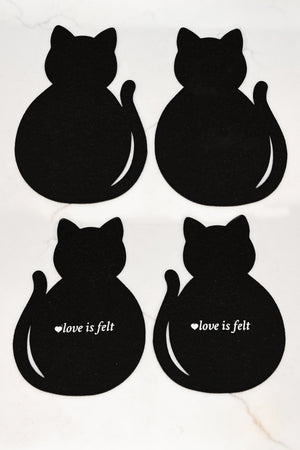 Four black cat-shaped felt coasters arranged in a 2x2 grid on a white marble background. The bottom two feature the white text 'love is felt' next to a small heart.